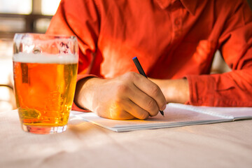 A guy with a glass of beer makes notes in a notebook while sitting in a cafe