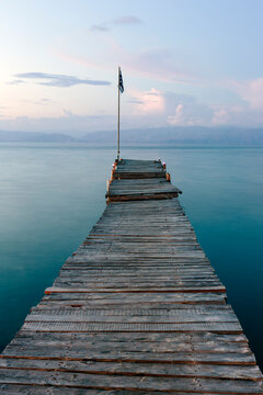 Wooden pier with a Greek flag at the end, looking out to sea just after the sun has set