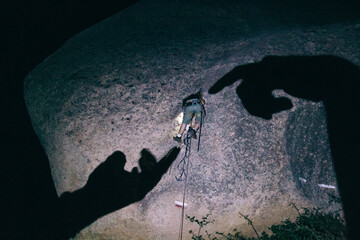 Shadow of a giant hands simulating the Creation of Adam with a climber on the middle while climbing at night on a rock