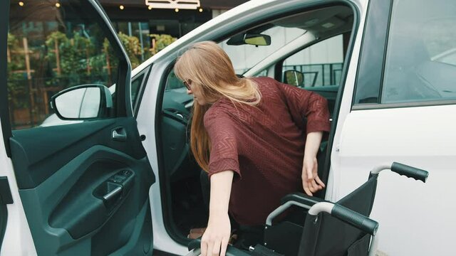 Young disabled woman getting out of the car in the wheelchair. High quality 4k footage