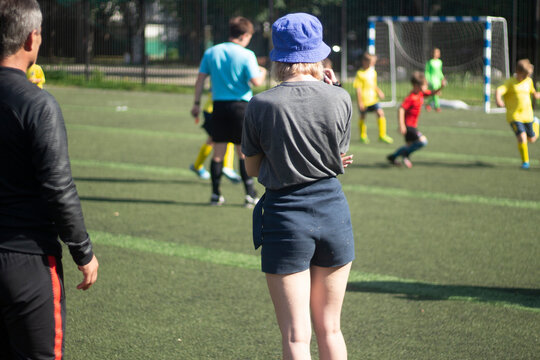 The girl takes pictures of sports. The girl is filming a football match. Girl in shorts on the playground.