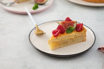 Piece of cheesecake with raspberries and figs on grey background.