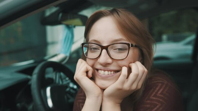 Close up, Face expression of young caucasian woman sitting on the driver seat. Face mask hanging on the mirror. High quality 4k footage