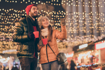 Two people couple girl point index finger x-mas evening tradition miracle outdoors lights hold eggnog beverage mug wear season clothes