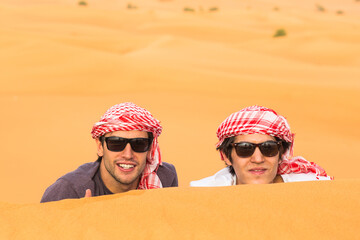 Two happy male tourists friends enjoying a safari tour in the Arabian desert sand dunes. Travel and...