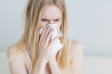 Sick woman with a cold blowing her nose into a tissue paper at home.
