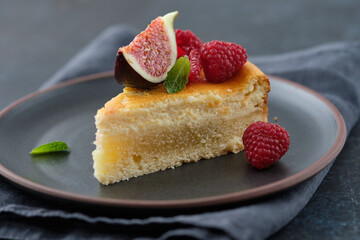 Piece of cheesecake with raspberries and figs on black background.