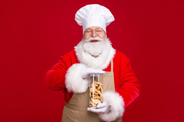 Photo of crazy white grey hair bearded santa claus hold ginger bread x-mas time eve cookies wear red costume apron isolated over bright shine color background