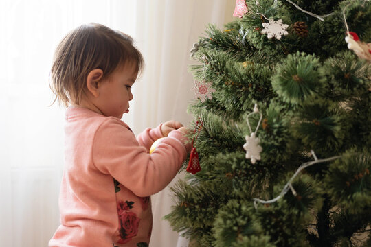 Toddler girl decorating christmas tree at home. December traditions for kids.