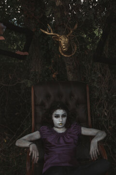 Girl painted in white sitting on an armchair at halloween