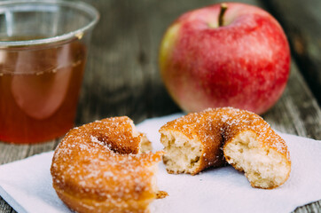 a broken cider dougnut on a napkin with an apple and cup of cider