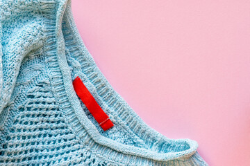 Warm knitted blue sweater with red label, pullover on a pink paper background with copy space