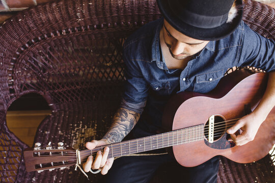 tattooed man in fedora playing guitar