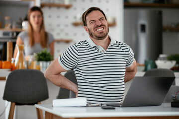 Young businessman having backache. Handsome man working at home.