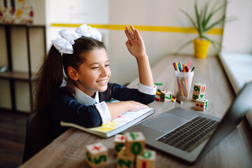 Beautiful school girl raises her hand to answer the teacher's question. School girl using laptop computer studying through online e-learning system. Distance learning. Covid-2019.