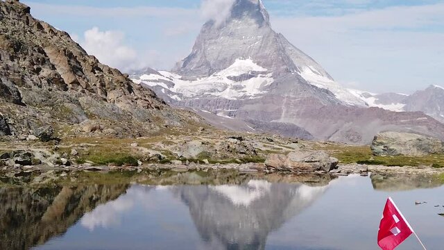 SLOW MOTION: Woman with Swiss flag at Mount Matterhorn or Mont Cervin, reflected on Riffelsee Lake. Tourism in Zermatt,Canton of Valais, Switzerland. Scenic landscape of popular tourist attraction