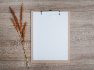 Blank clipboard with dry flowers decoration on wooden desk background.