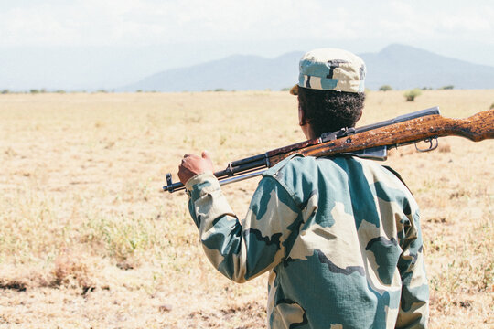 African man with a rifle and military garment on the savanna while a safari