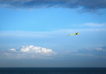 yellow kite against a blue sky with a few clouds above the sea