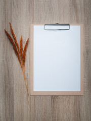 Blank clipboard with dry flowers decoration on wooden desk background.