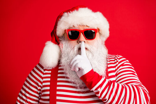 Close-up portrait of his he nice handsome mysterious white-haired Santa wearing sunglasses showing shh sign silence silent mute isolated over bright vivid shine vibrant red color background