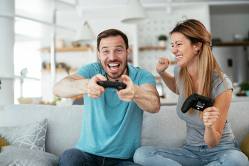 Naklejka premium Boyfriend and girlfriend playing video game with joysticks in living room. Loving couple are playing video games at home..