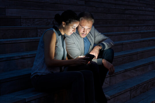 Couple regardant l'écran d'un smartphone dans la rue en pleine nuit