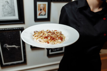 carbonara pasta with lots of cheese on a white plate. Waiter with a plate of carbonara pasta