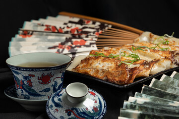 Material of traditional chinese fried dumplings(also called gyoza,pot sticker) on table with black background and decorate with chinese style fans and tea cup.
