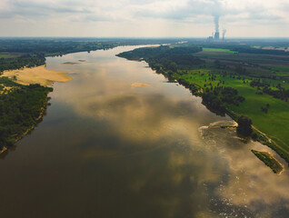 Naklejka na ściany i meble Large river flows through meadows and fields with power plant in a distance. Drone, aerial view