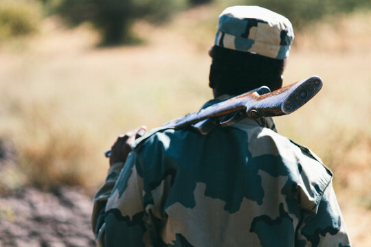 African man with a rifle and military garment on the savanna while a safari
