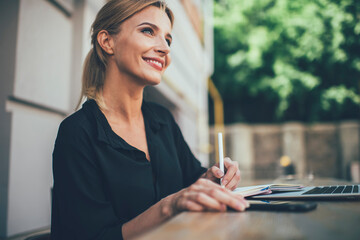 Happy female student with cute smile on face studying information notes learning at outdoors table desktop, cheerful Caucasian woman 20 years old enjoying accounting with education textbook