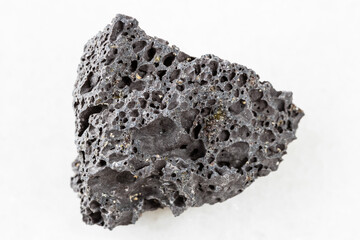 closeup of sample of natural mineral from geological collection - rough black Pumice rock on white marble background