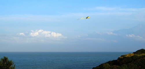 yellow kite against a blue sky with a few clouds above the sea