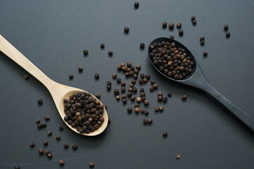 Top view of peppercorns in wooden spoon placed on black background.