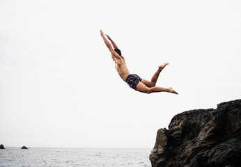 Young brunette fitness man jumping into water from a rock or a cliff