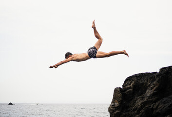 Young brunette fitness man jumping into water from a rock or a cliff
