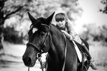 Cute little girl with long hair riding a horse outdoors. Pet therapy