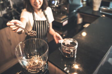 Blurred portrait of a barista Asian woman Scooping roasted coffee beans into a coffee grinder, This picture focuses on the coffee and spoon, to drink and work concept.