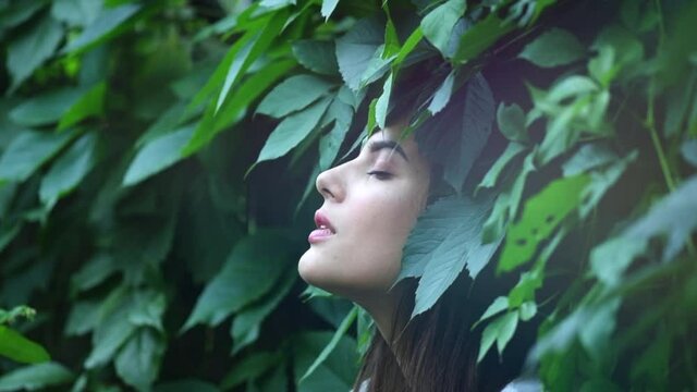 Beautiful fashion model woman enjoying nature, breathing fresh air in summer garden over Green leaves background. Harmony concept. Slow motion 4K UHD video