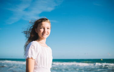 Cheerful girl standing against waving sea on sunny weather