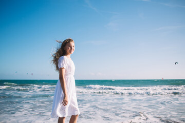 Fototapeta na wymiar Happy stylish girl standing on beach against waving sea