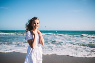 Fototapeta na wymiar Cheerful girl in white dress standing on seashore