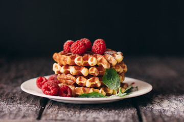 yummy belgian waffles with raspberries and mint leaves on wooden table