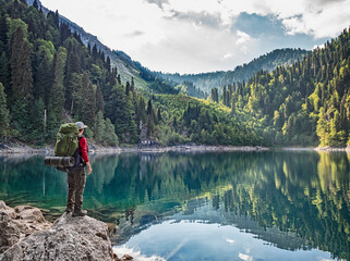 Active tourist with backpack standing at Lake Smaller Ritsa background in Caucasus Mountains in Abkhazia