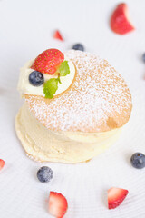 Fluffy souffle pancakes with cream and berries on white plate set on cafe table.