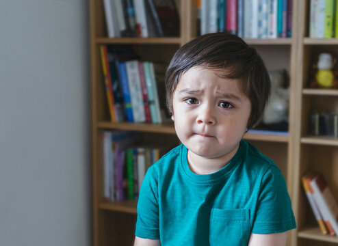 Emotional Portrait Sad Kid Looking At Camera With Unhappy Face, Angery Little Boy Sitting Alone With Blurry Bookshelf Background, Portrait Upset Child, Spoiled Children Concept