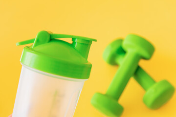 Pair of green dumbbells and  bottle for water on yellow background. Healthy lifestyle, fitness...