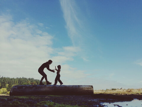 young mom playing with child on log out side in nature - big blue sky