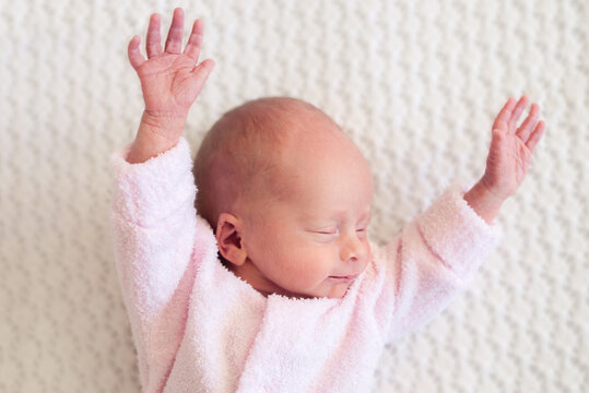 Newborn baby girl with outstretched arms wearing a pink terry cloth onesie